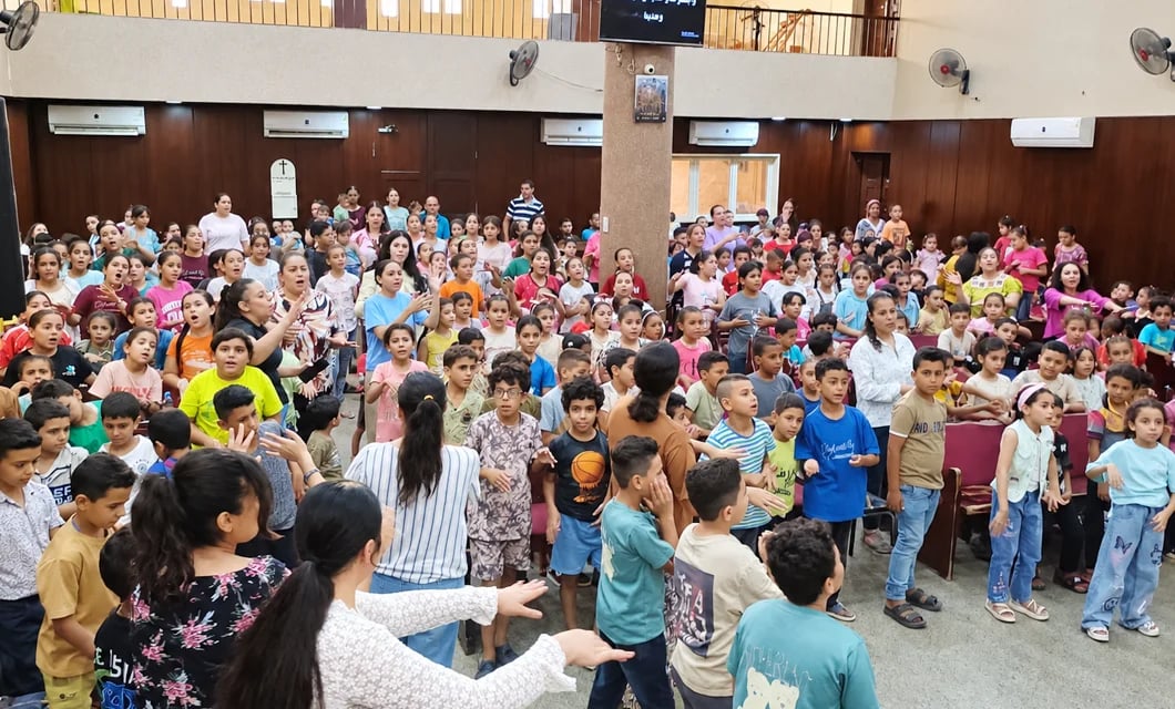 A large group of children singing and worshiping together inside a church hall in Egypt